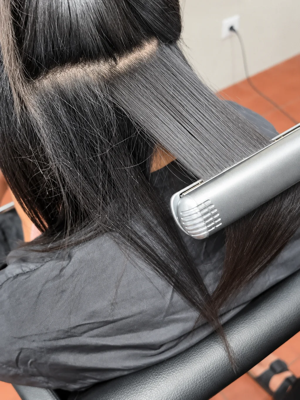 Mechón de pelo oscuro y liso pasando por una plancha en el salón, con la clienta sentada de espaldas